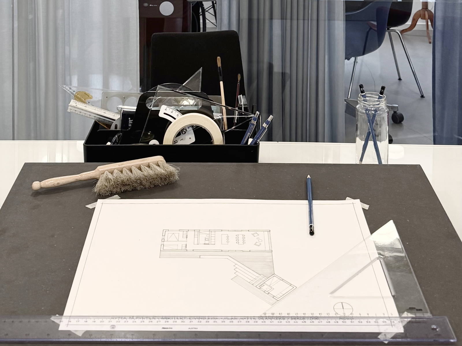 Foto av tegnebord med en arkitekt tegning og diverse tegneredskaper rundt.