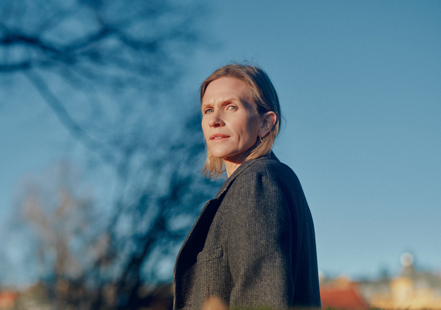 Portrett foto av Inger Therese Hoff, blå himmel bak og en hekk fremfor.