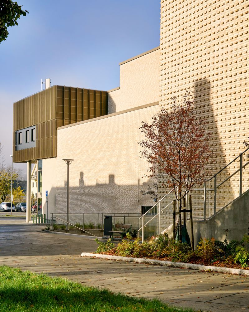 Fasade foto av Steinkjær kulturhus, lys teglstein og gylne fasade plater i ulike volumer. 
