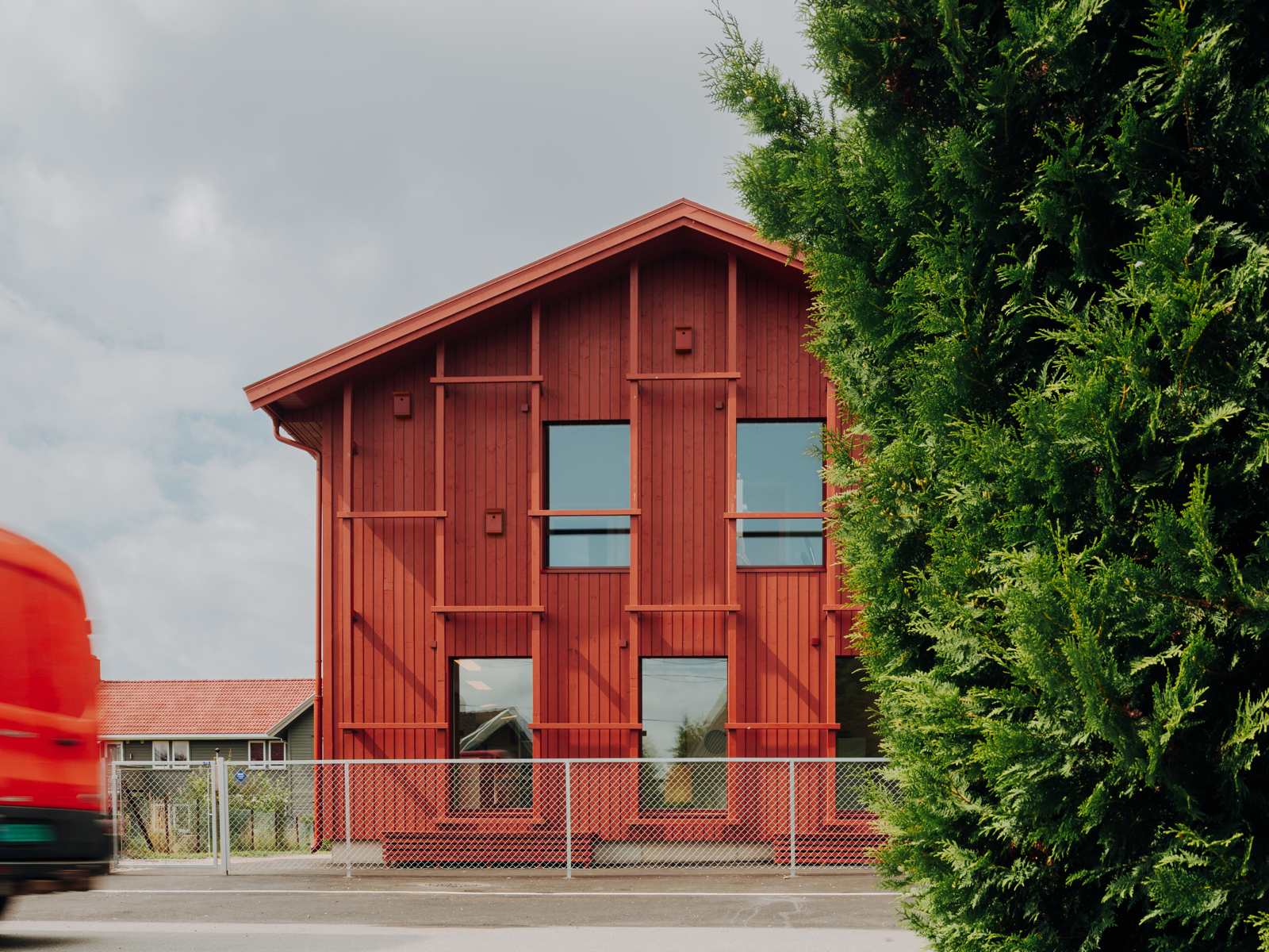 Fasade foto av Alvim barnehage, rød gavl vegg, tre og vei med en bil som kjører fremfor.