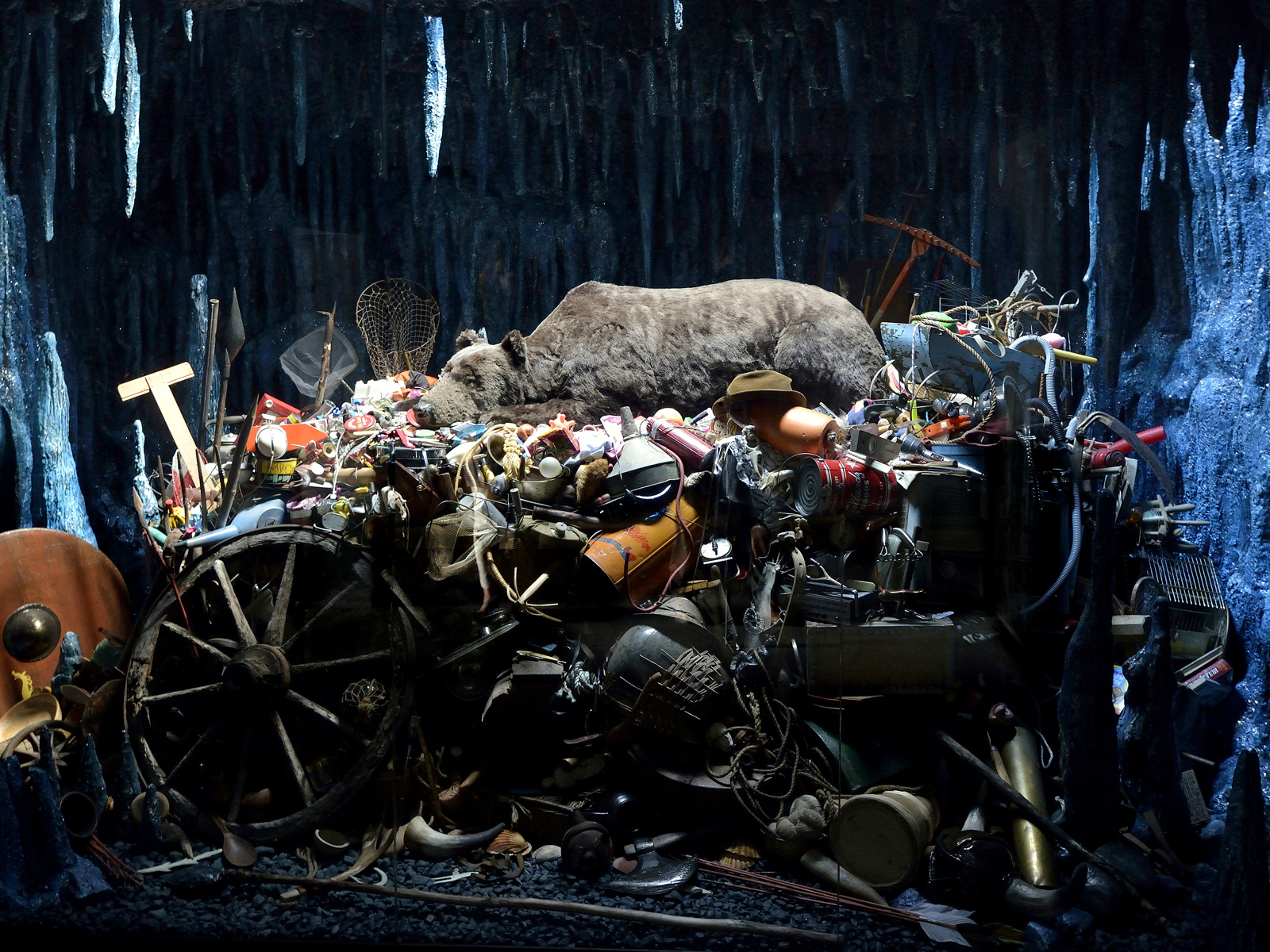 En bjørn ligger på toppen av en haug med diverse søppel inne i en hule. Foto.