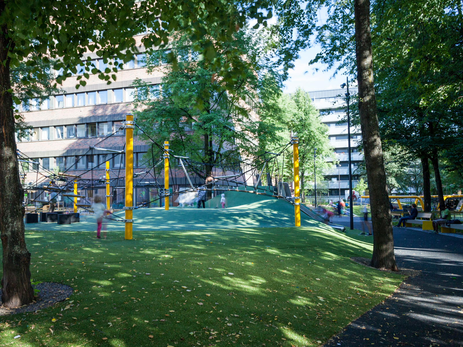 Lekepark mellom bygg, barn leker i klatrenett. Foto.