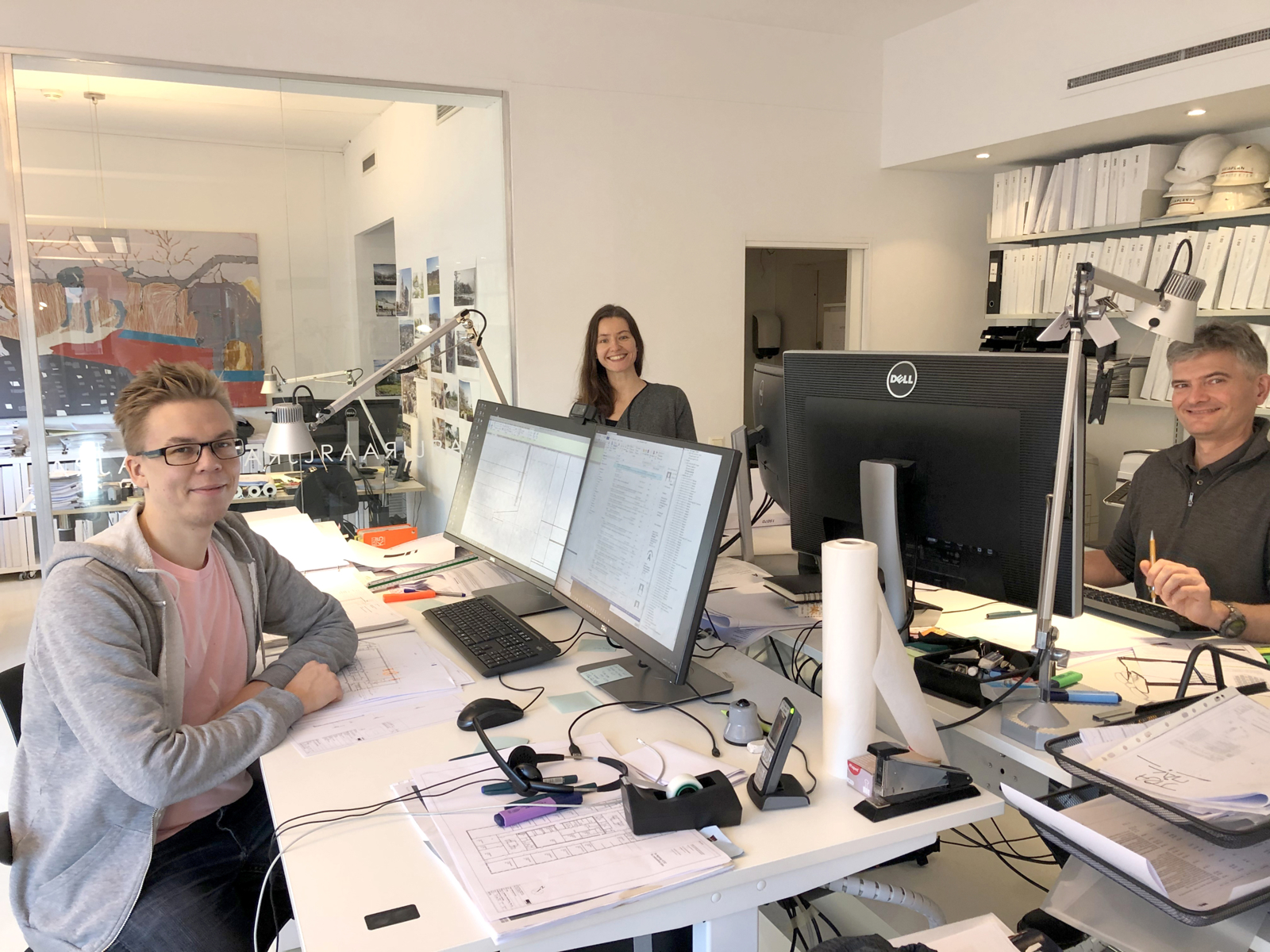 Tre personer ser opp fra kontorpultene