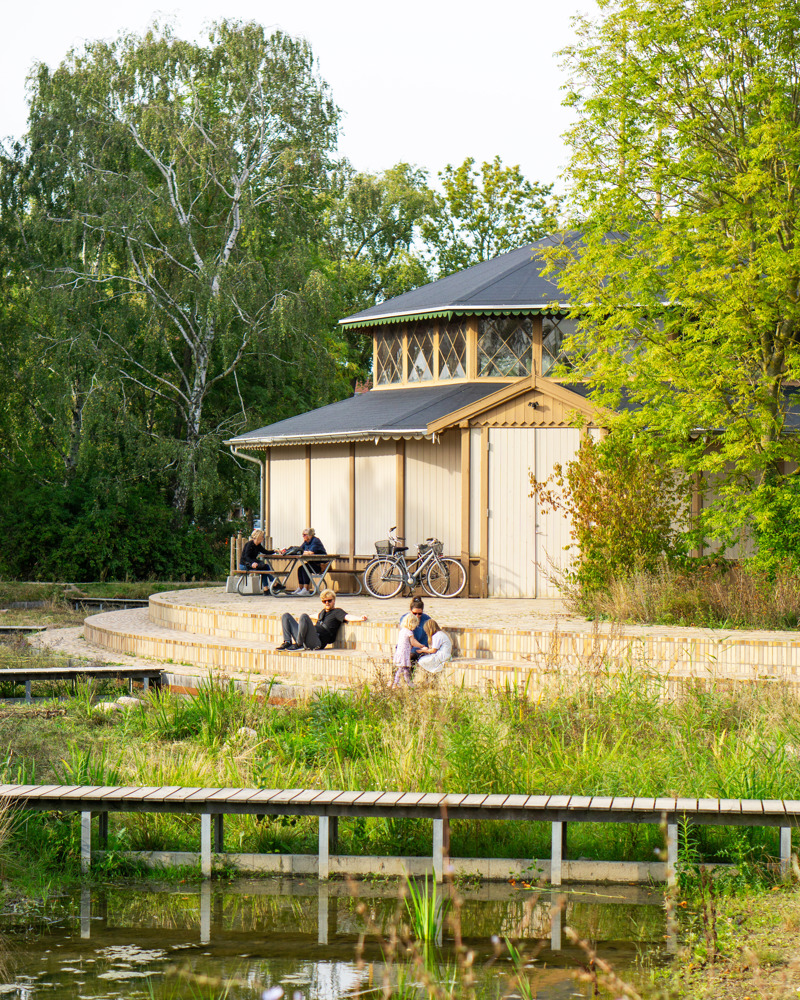 Foto av lysthus i en grønn park, mennesker som sitter rundt om.