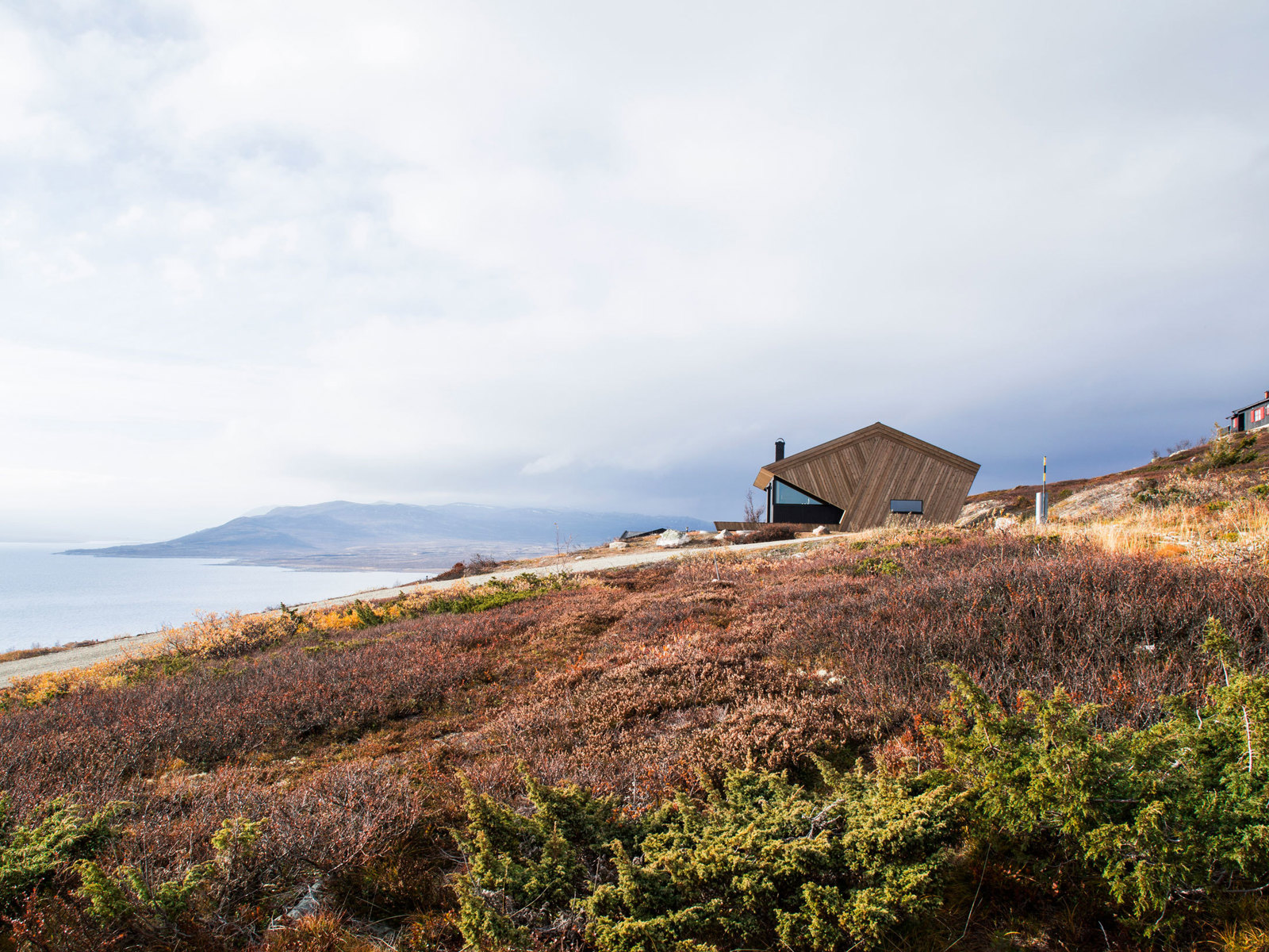 Hytte sett på avstand over lyng og med en fjord og fjell i bakgrunnen