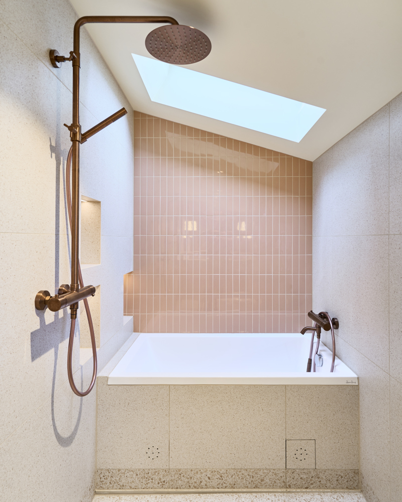 Interiørfoto av dusj og badekar med lyse fliser, rosa fliser på den ene veggen over baderkaret. Takvindu over badekar