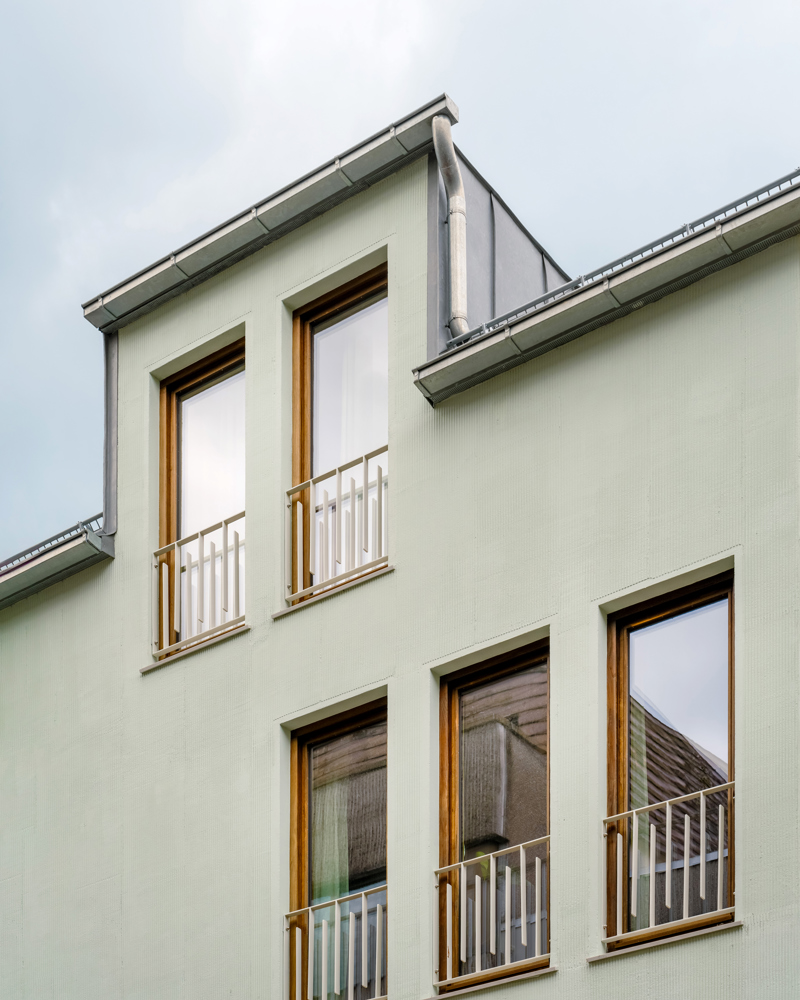 Foto tatt opp på fasade av grønn enebolig, blå himmel i bakgrunnen.