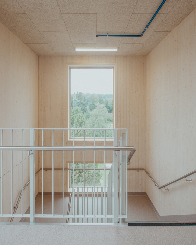 Foto av trappeoppgang i lyst treverk og med store vinduer som slipper inn mye naturlig lys.