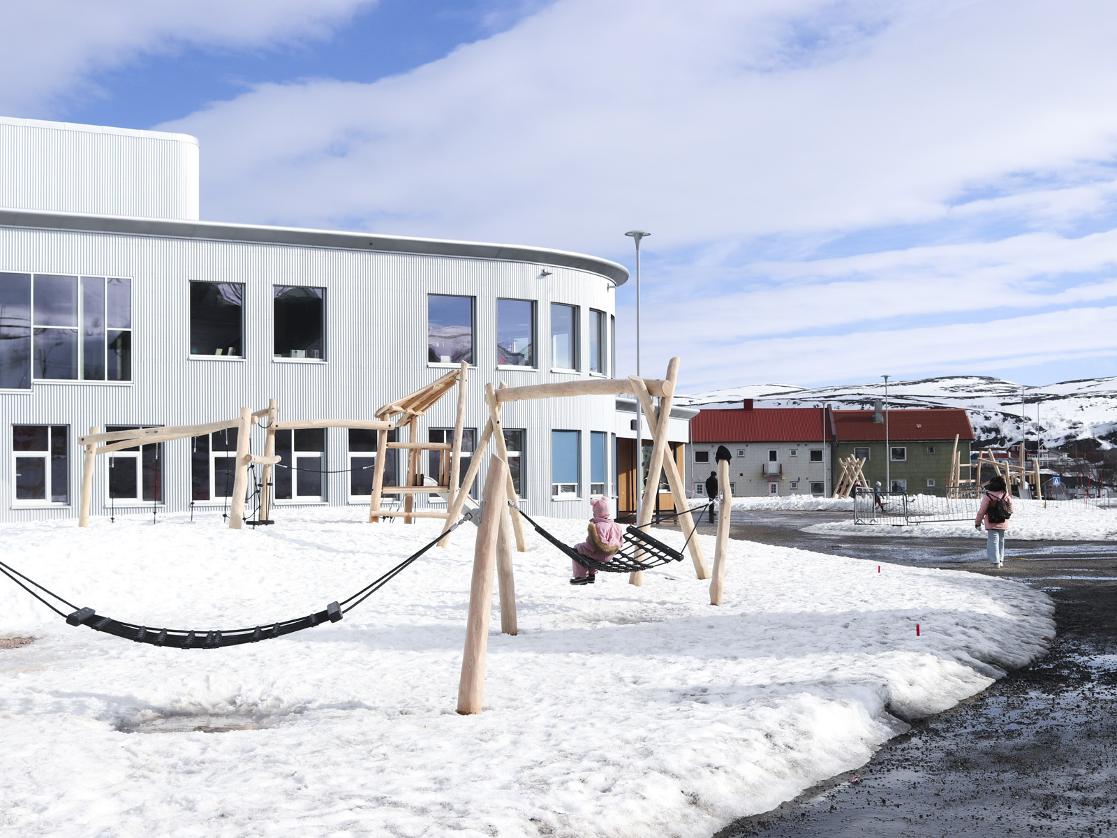 Foto av skolegård med snø og 2 etasjers kurvet skolebygg.
