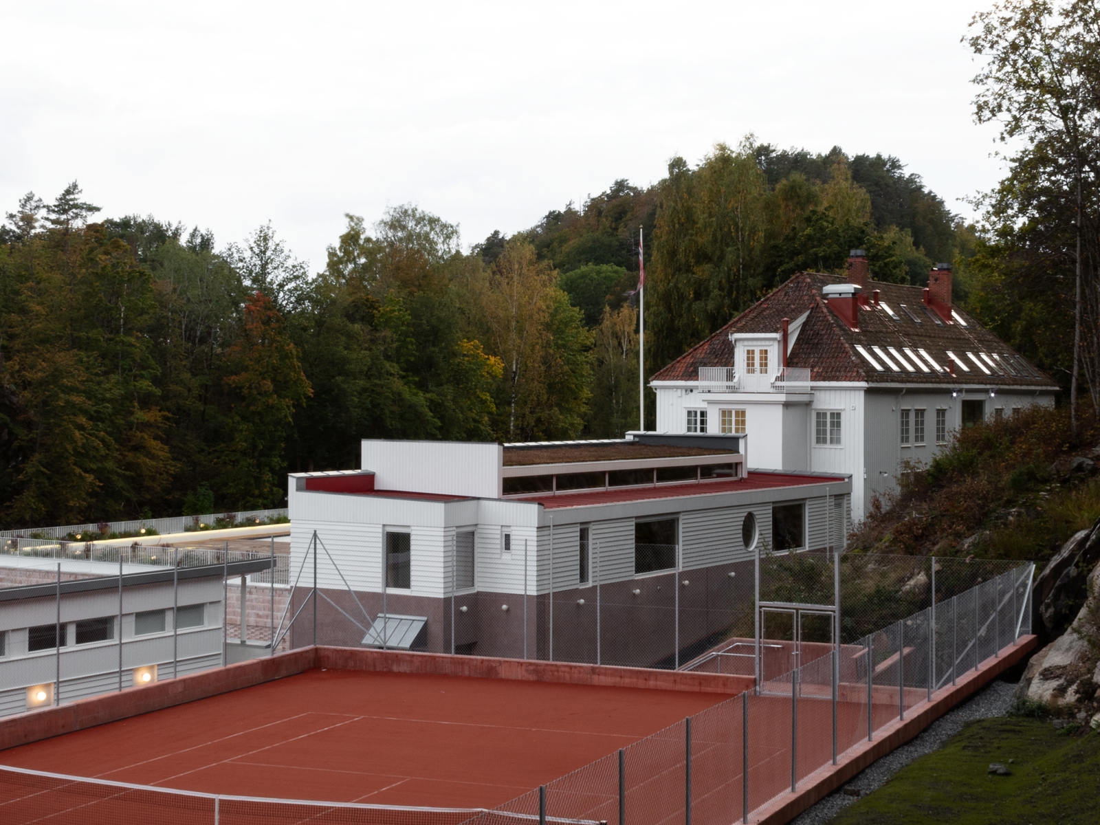 Foto av resort med tennisbane og flere hvitmalte bygg med høst trær rundt.