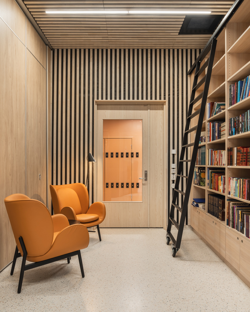 Interiør foto av bibliotekrom, oransje stoler og evart stige på skinner langs bokhyllen.