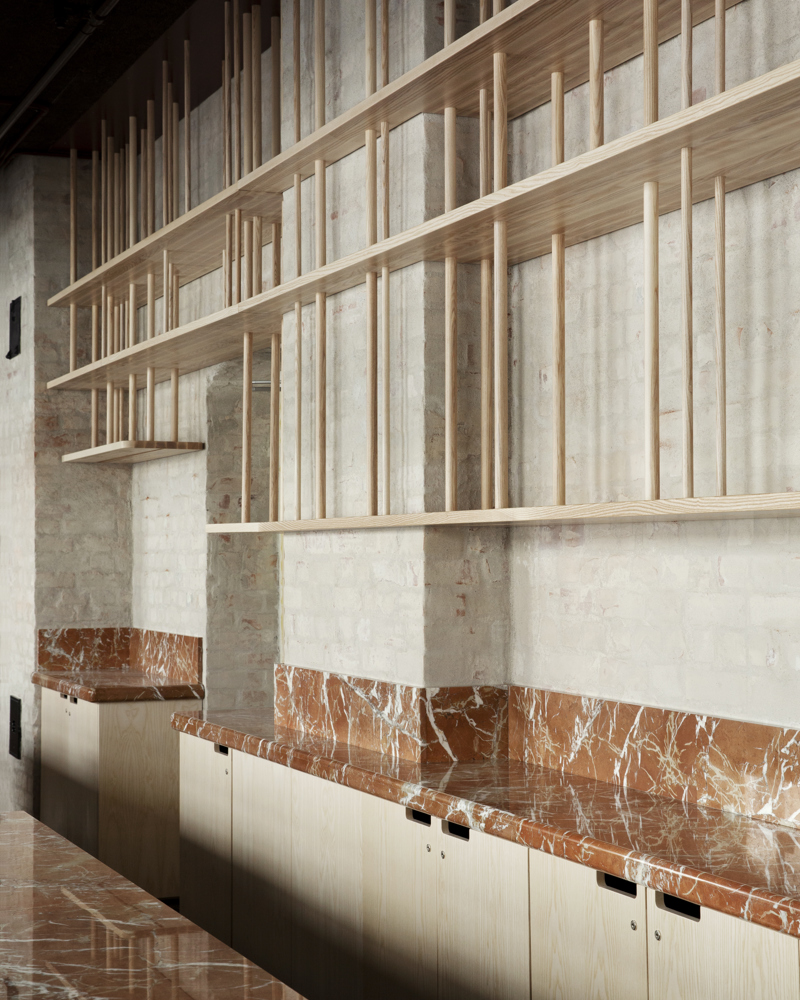 Kjøkken og bardisk i rød stein, med hyller i ask som henger ned. Interiør. Foto.