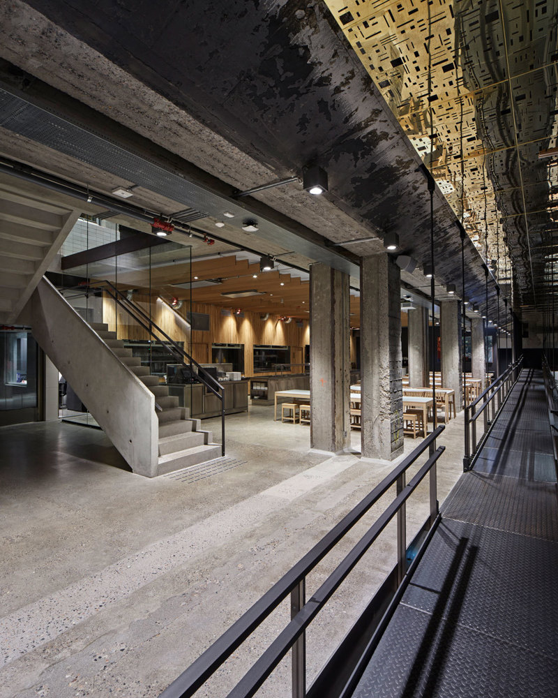 Interiør fotografi av bygg med flere sittegrupper, reflekterende gullplater i taket, betong trapp i bakgrunnen.