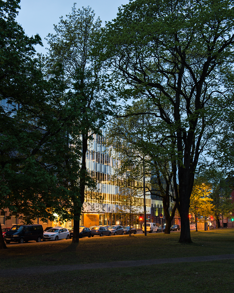 By fotografi i kveldsmørket, bygg med en opplysende fasade i bakgrunnen.