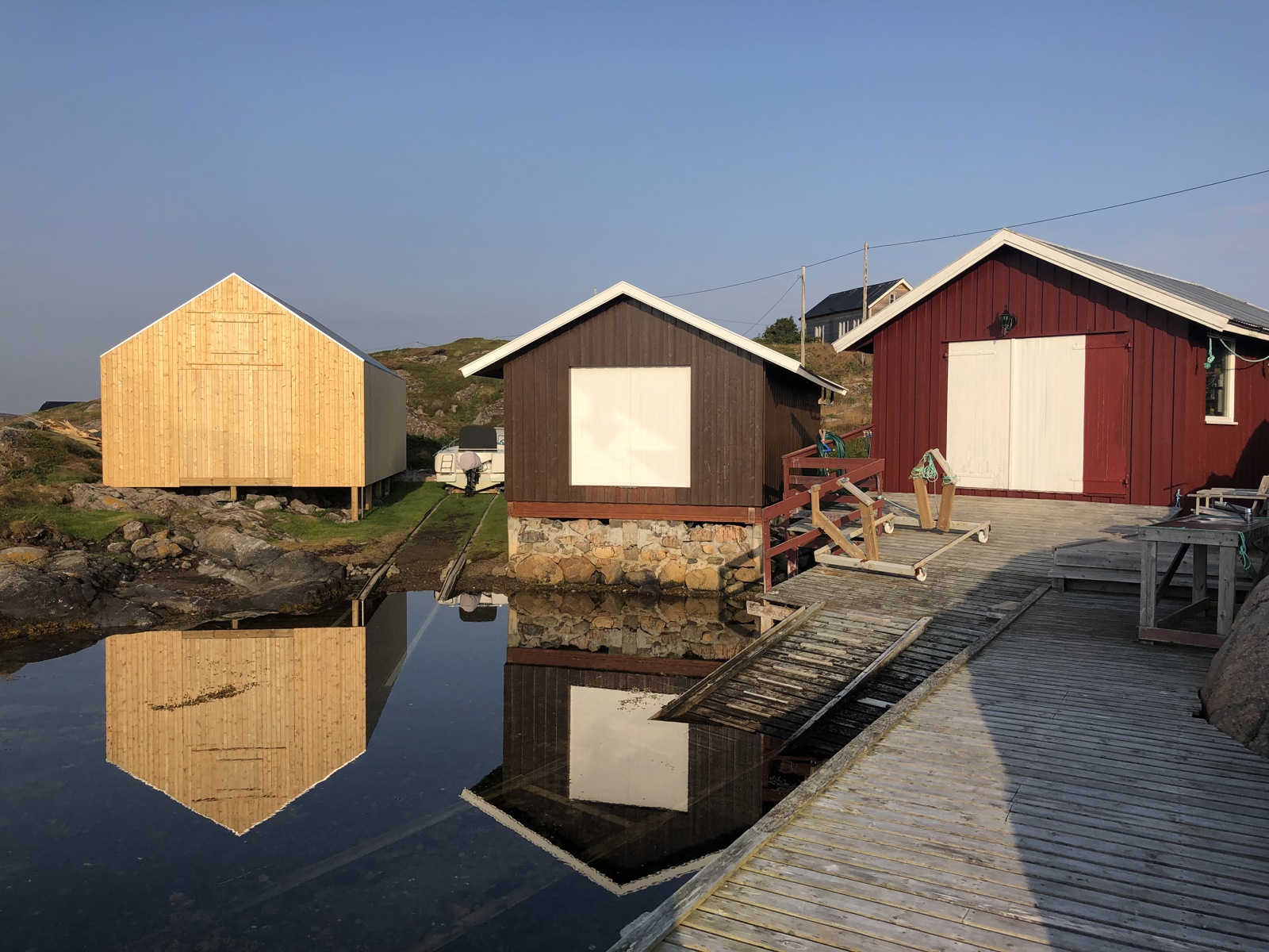 Foto av tre naust liggende langs vannkanten.