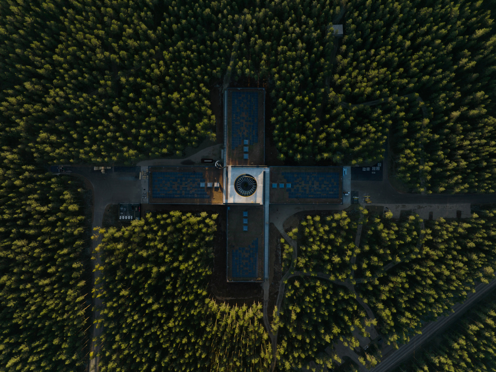FLy/dronefotografi som viser fabrikk bygg formet som et plusstegn i skogen. Foto.