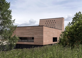 Spikkestad kirke avbildet utenfra, med grønn eng i forgrunnen og trær på sidene.