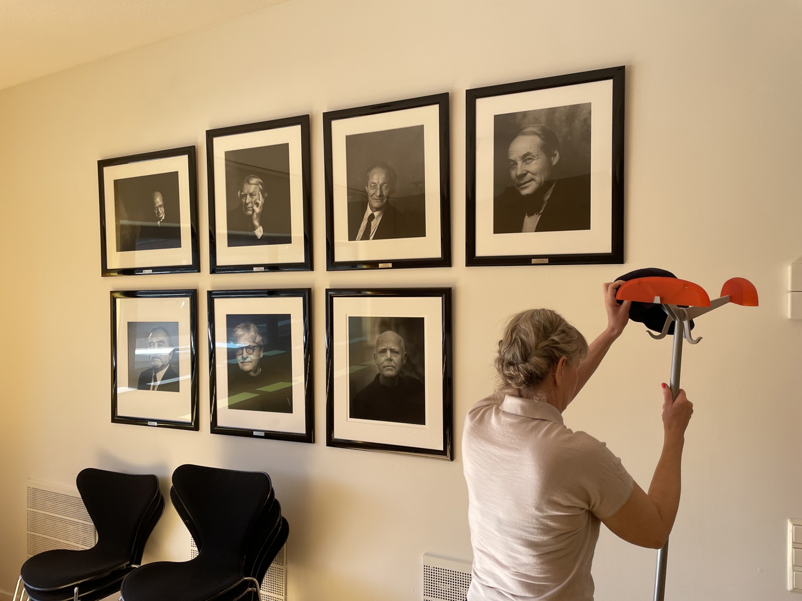 AHO-rektor Irene Alma Lønne flytter en stumtjener foran en vegg med bilder av tidligere AHO-rektorer.