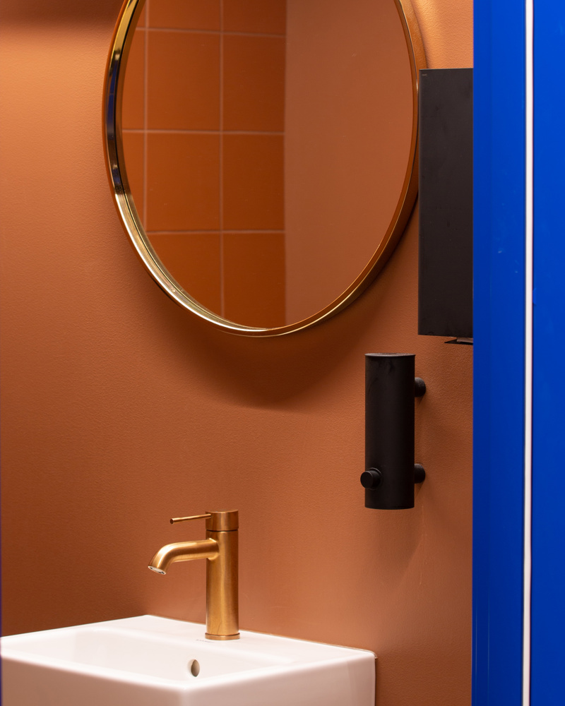 Vask og speil, oransje vegg. Foto.