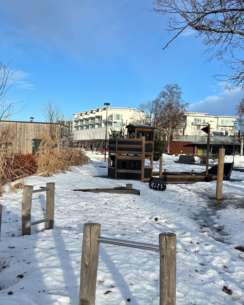 Foto av parkområde dekket i snø, blokker i bakgrunnen.