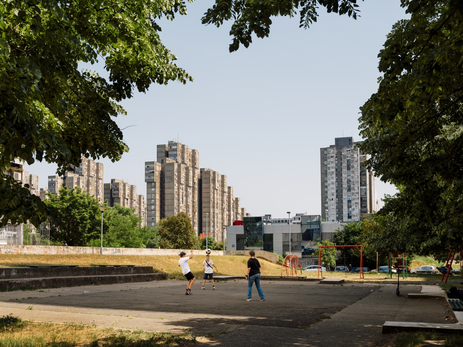 By i bakgrunnen med skyskrapere i betong, i front barn som leker på et uteområde. Foto.