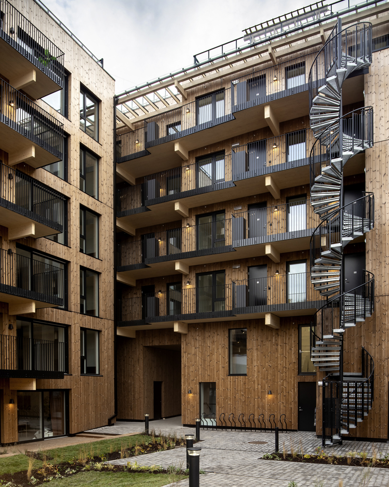 Bakgård rammet inn av bygg med fasader i tre og svarte detaljer. Foto.