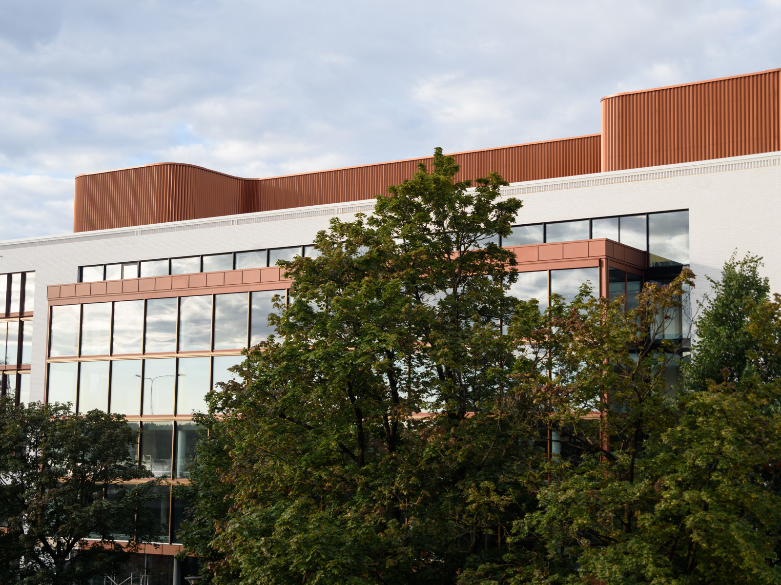 Fasadefoto av kommunegården i Sandvika, trær i forgrunn, bygg i hvit og oransje i bakgrunnen.
