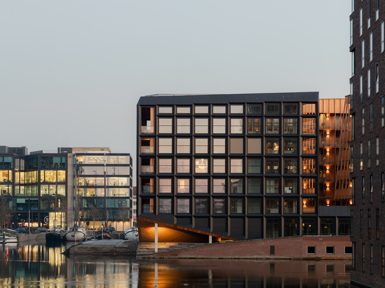 Foto av havneområde med boligbygg i varmt kveldslys, vann, båter og boligblokker.