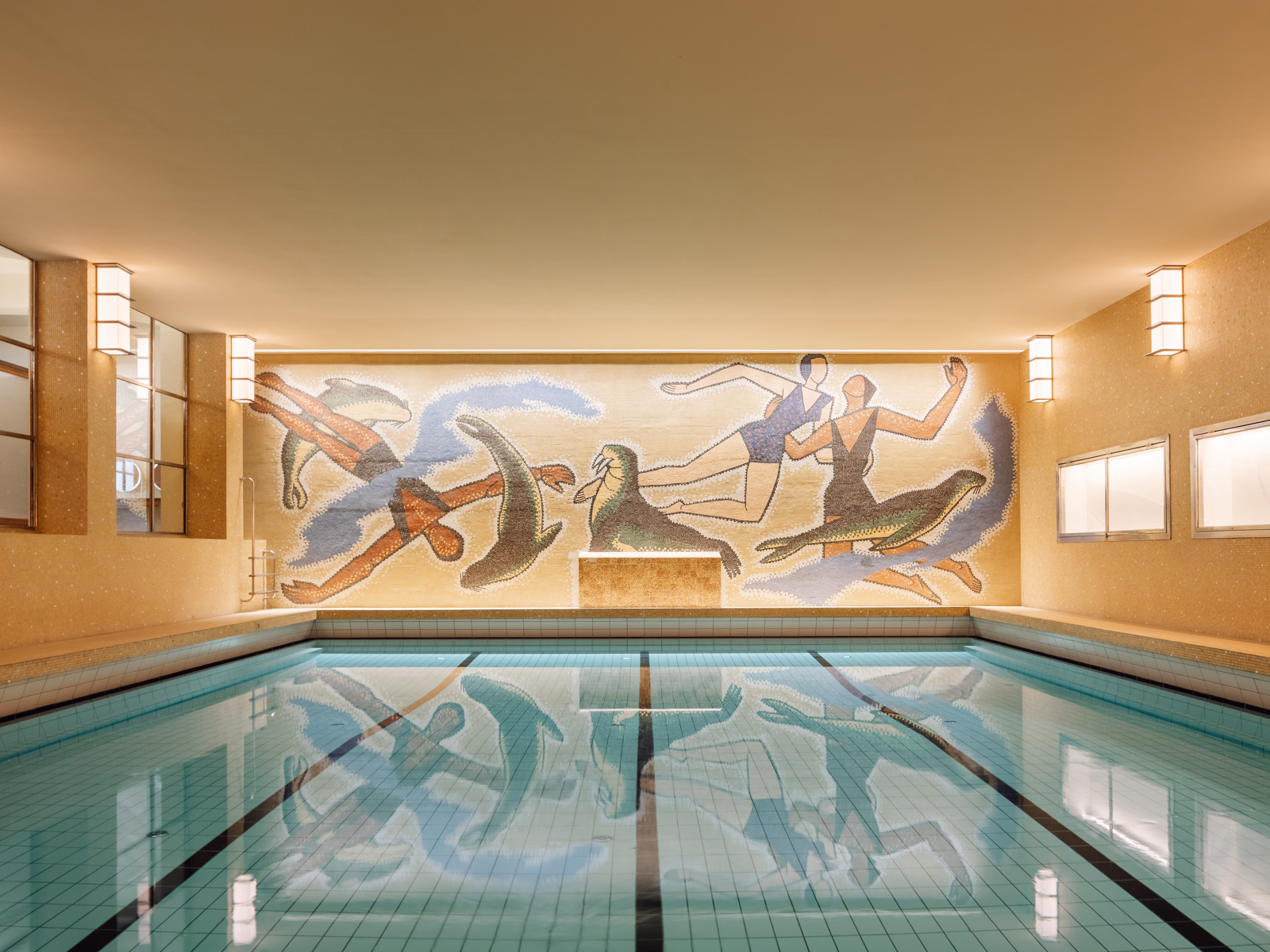Badebasseng med kunst på veggen og varmt lys. Foto.