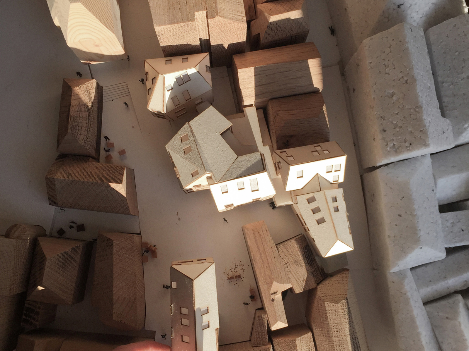 Arkitekturmodell med en hånd som plasserer et trehus blant andre trehus i en isopormodell. Foto.