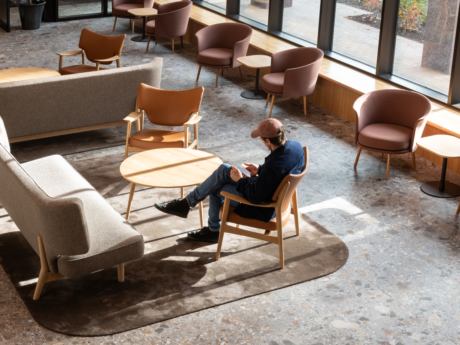 Interiørfoto av Tønsberg Tinghus som viser en mann som sitter i venteareal for publikum. Gulvet er i grå terazzofliser, møblene er i tre, skinn og stoff i duse farger. 