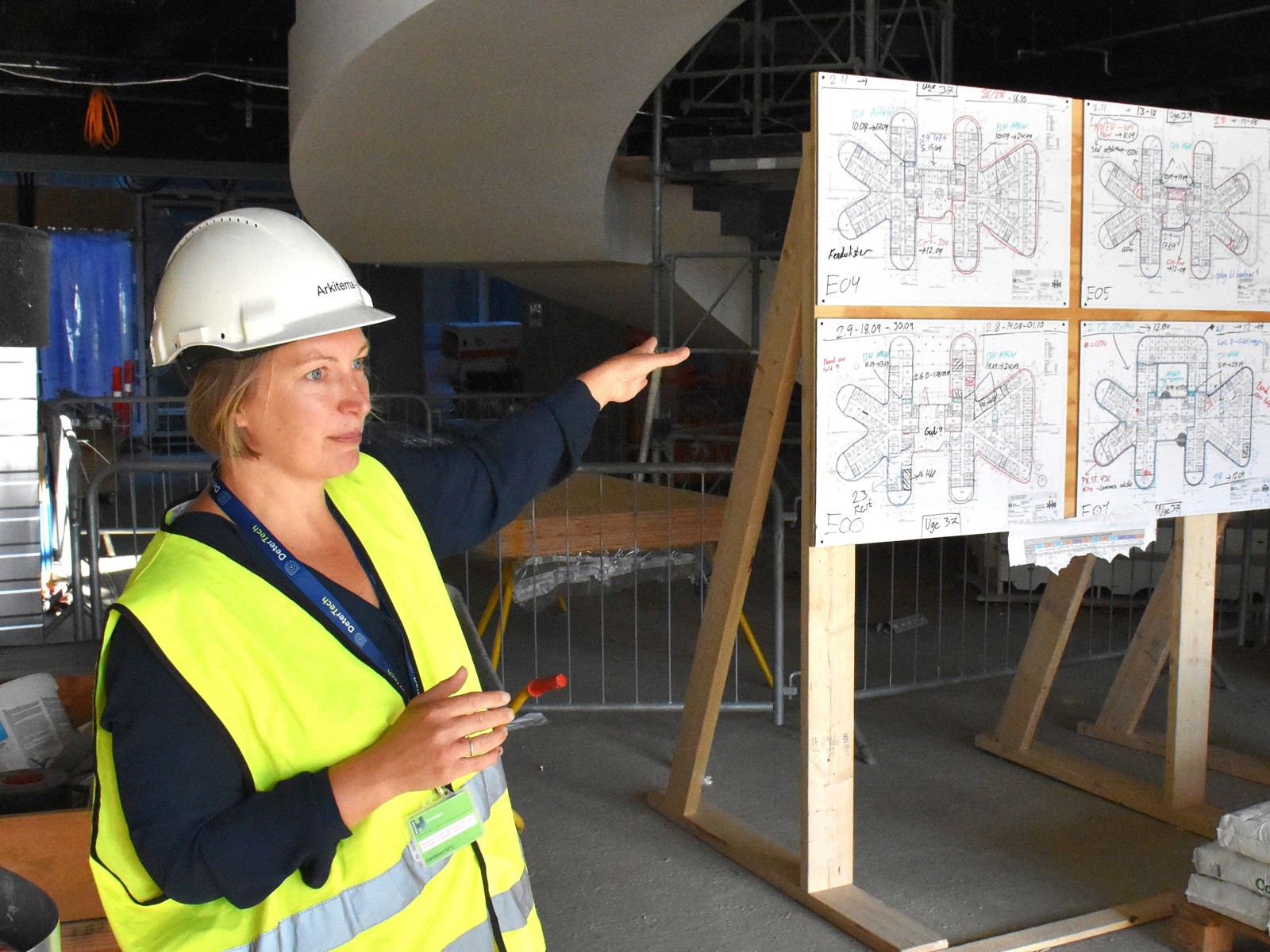 Foto av Pernille Birkel Fagerstrøm som peker på en vegg med planer på byggeplass.