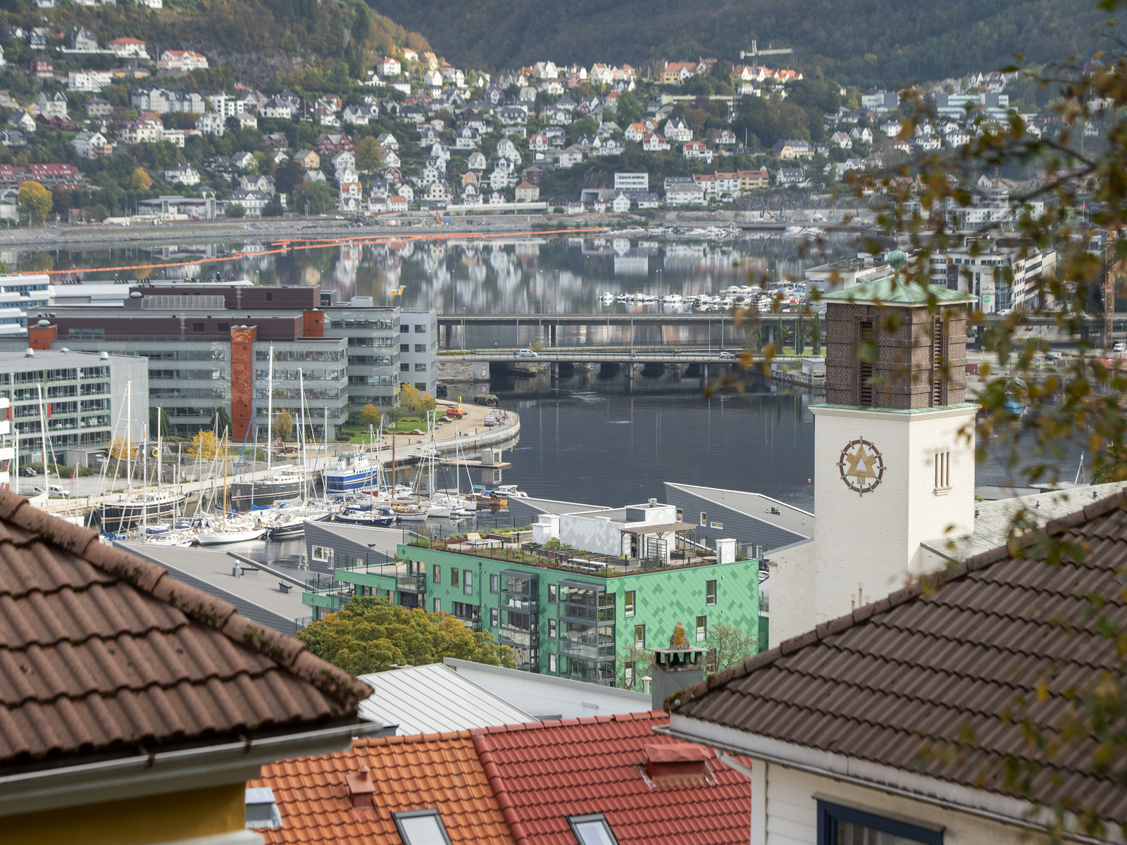 Utsikt over hustak, by, bro, kirketårn og hav i bakgrunnen. Foto.