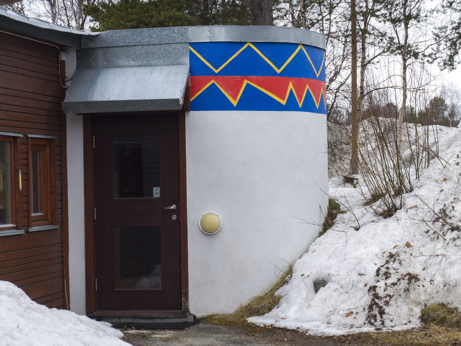 Foto av kurvet inngangsparti med samisk maling, snø rundt.