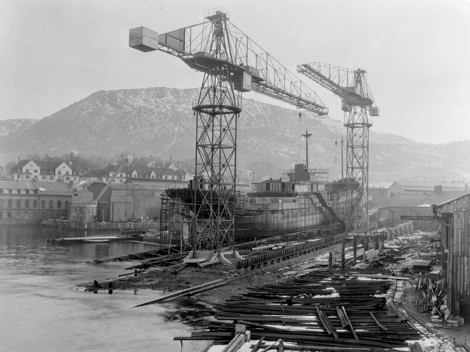 Svart hvitt bilde av havneområde med store heisekraner. Foto.