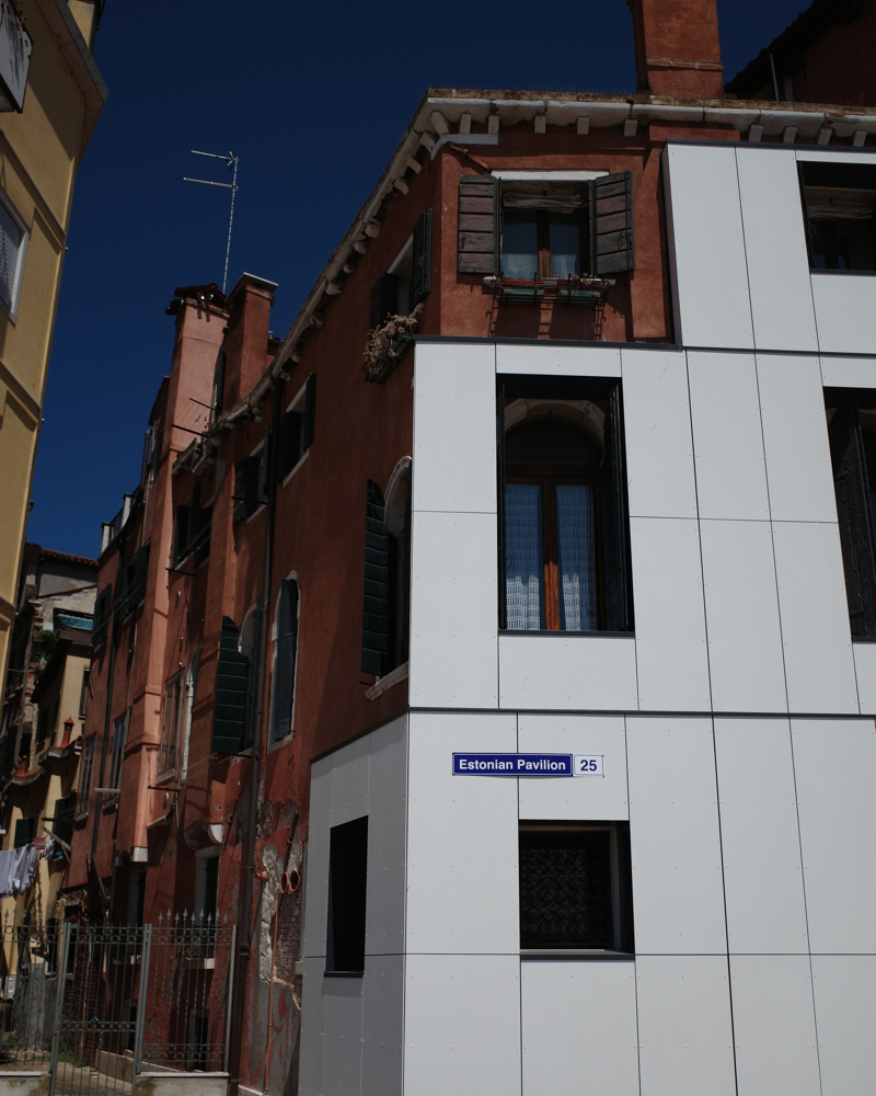 Foto av et gatehjørne i Venezia med et tradisjonelt bygg delvis kledd i plater.