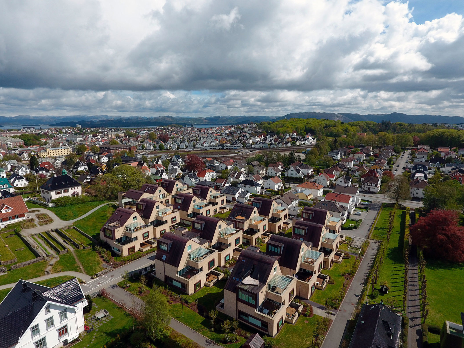 Oversiktsbilde av boligområde med lignende hus i lys teglstein. By i bakgrunnen. Foto.