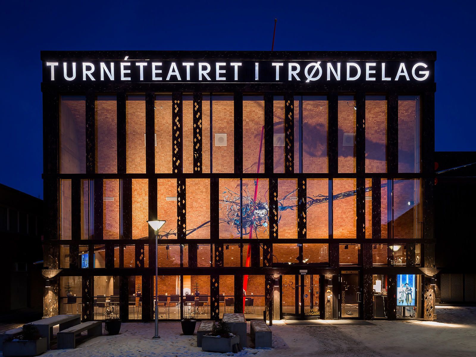 Eksteriør, framside, en glass-fasade som lyser frem i mørket.