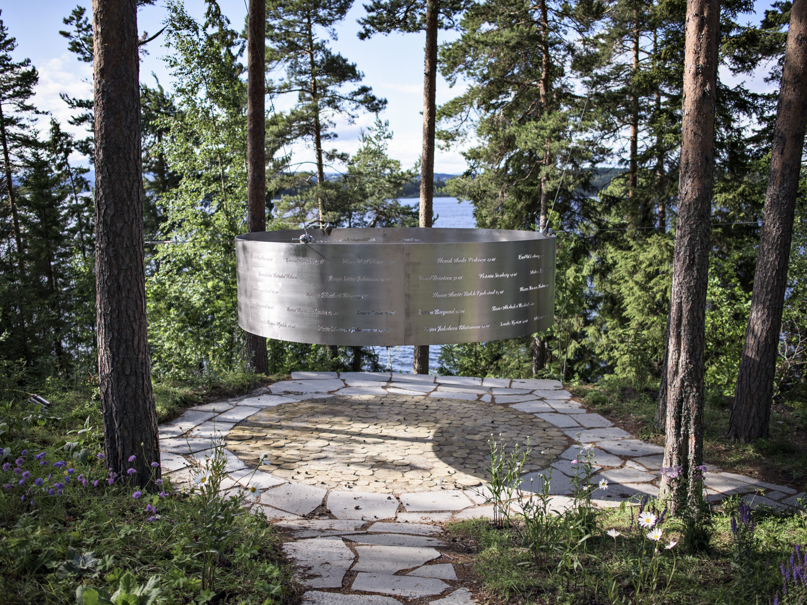 Rund minnevegg hengende over rund plass i skogen. Foto.