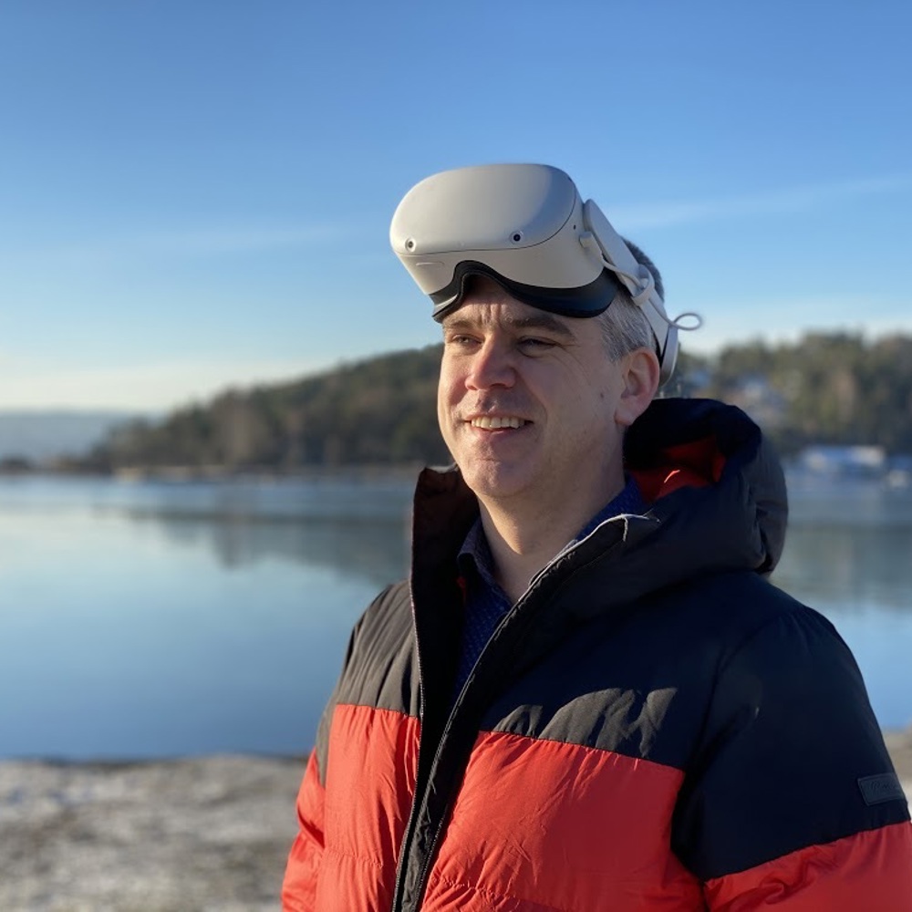 En mann som står ved en innsjø med VR-briller på