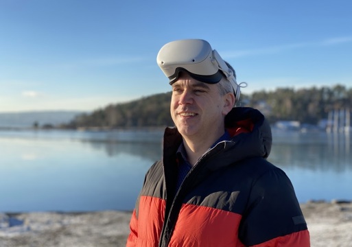 En mann som står ved en innsjø med VR-briller på