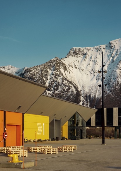 Eksteriørfoto av anlegget som viser et gult og et orange bygg, mens et snødekket fjell stekker seg opp i bakgrunnen