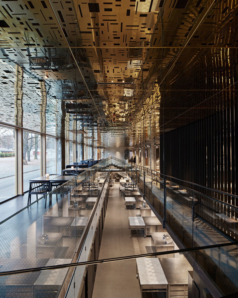 Interiør fotografi av bygg med flere sittegrupper, åpent ned til etasjen under, reflekterende gullplater i taket.