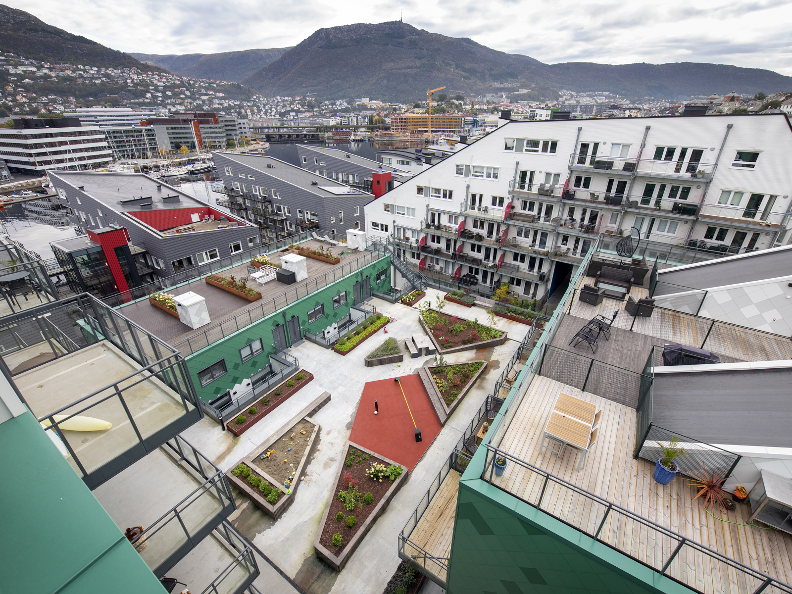 Foto fra takterrasse ned til felles bakgård med grønt og veier, i bakgrunnen by. 