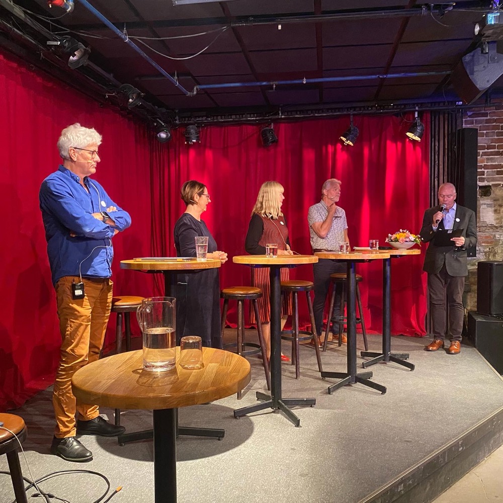 Foto av mennesker som står på en scene og snakker sammen.