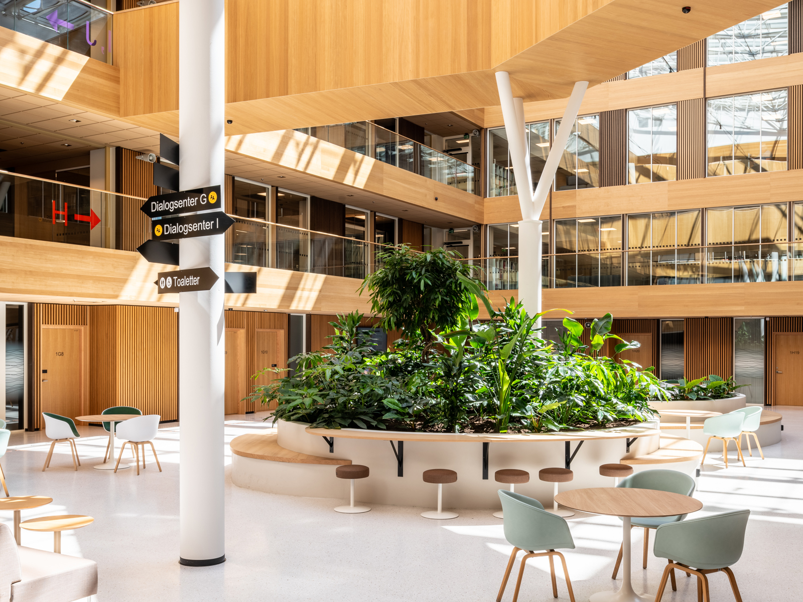 Interiør foto av innendørs atrium med glasstak i kontorbygg, sittegrupper og innendørs gangbro.