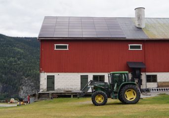 En traktor foran en gammel gårdsbygning med solcelleanlegg på taket. Foto.