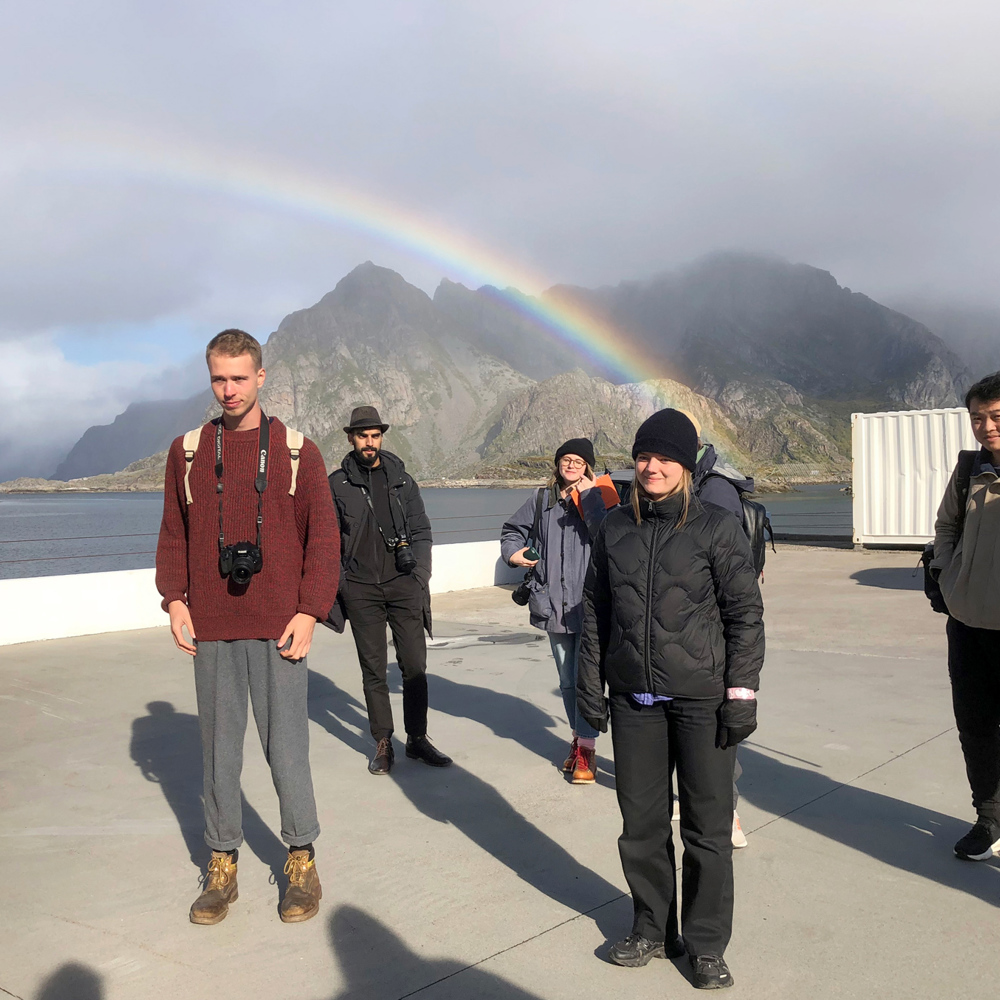 Studenter på brygge, fjell og vann i bakgrunnen. Foto.