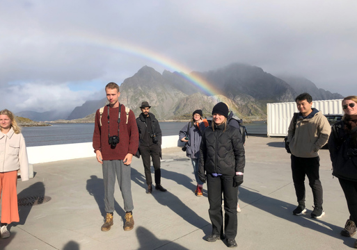Studenter på brygge, fjell og vann i bakgrunnen. Foto.