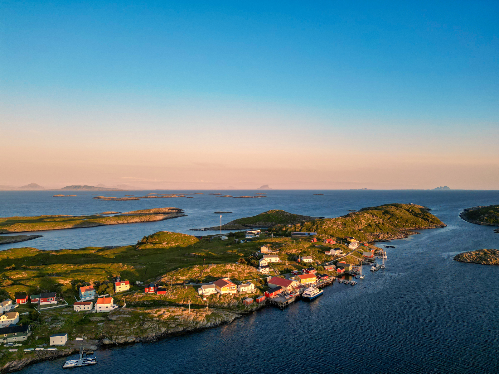 Dronefoto av grønn øy med noen små hus på. 